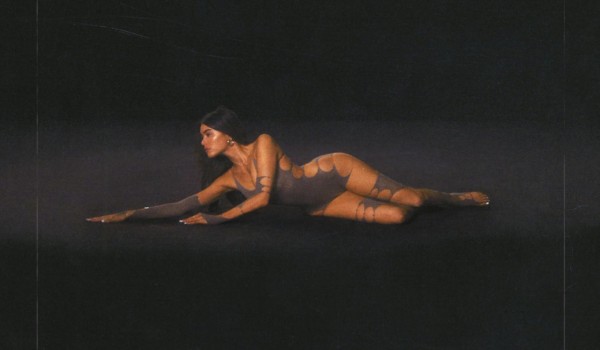 Madison Beer stretched out along a black floor in a grey bodysuit
