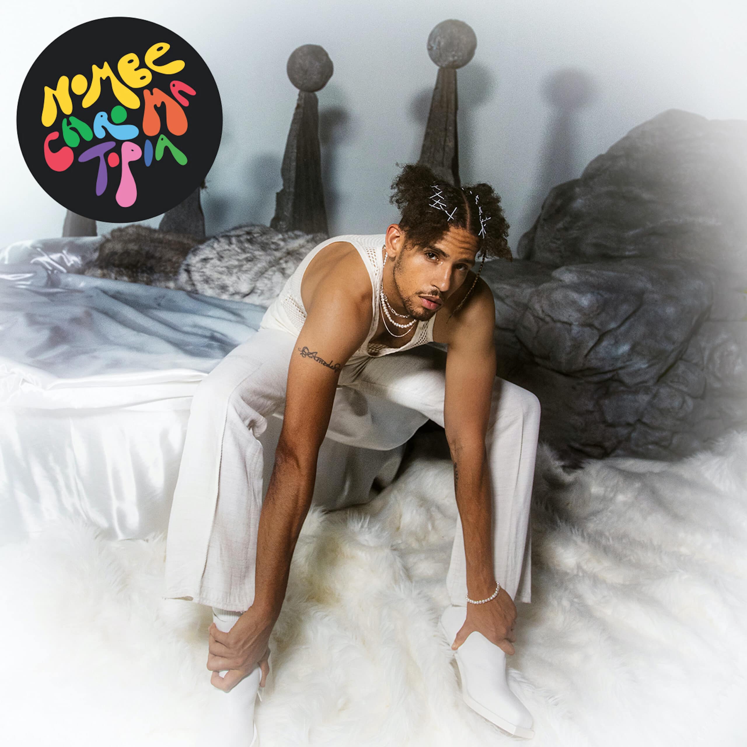 NoMBe sitting in a bed of white sheets while wearing all white.