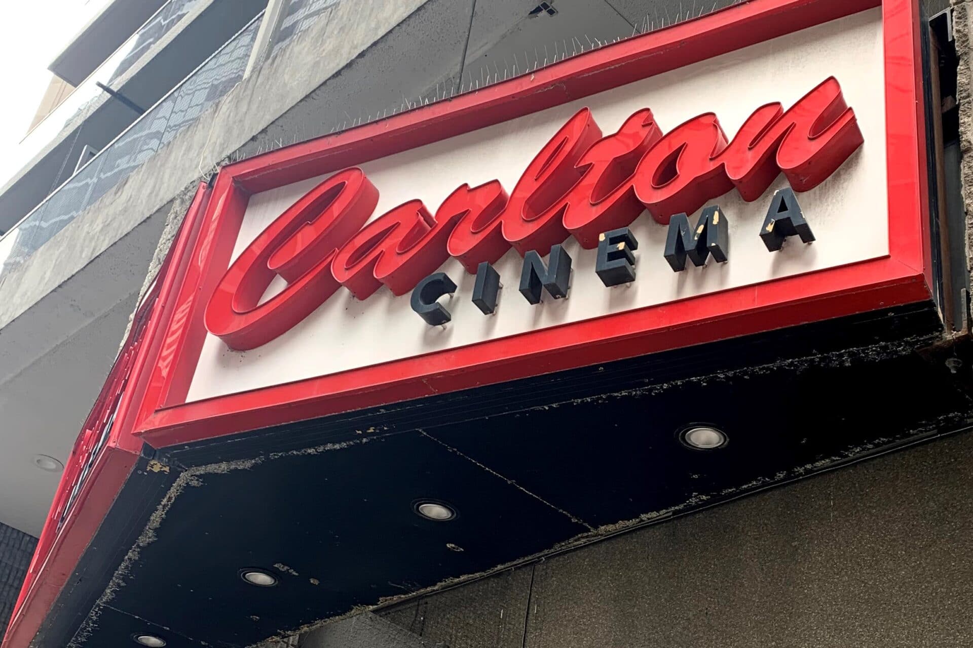 Red and black letters on a white sign on an elevated wall outside.