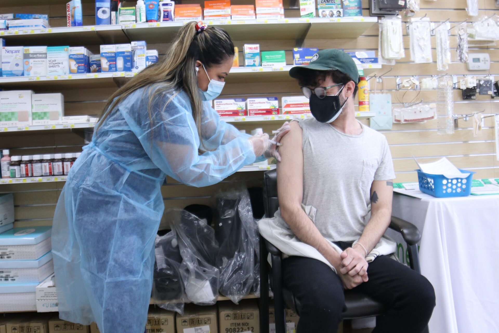 A person is sitting down while a person standing gives them a needle shot inside a clinic