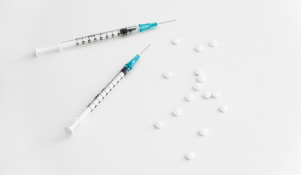 White pills and two syringes scattered on a white table.