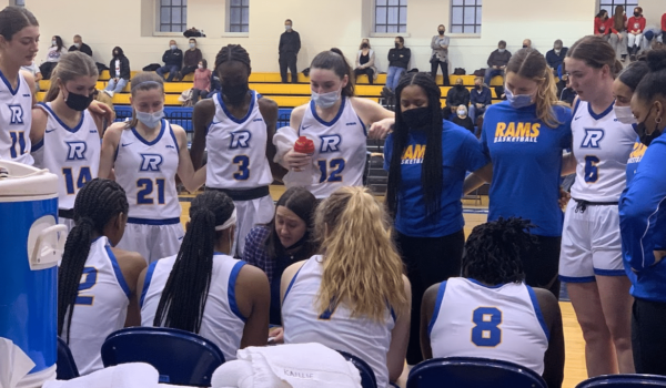 People in white basketball jerseys in a close huddle on a team bench.