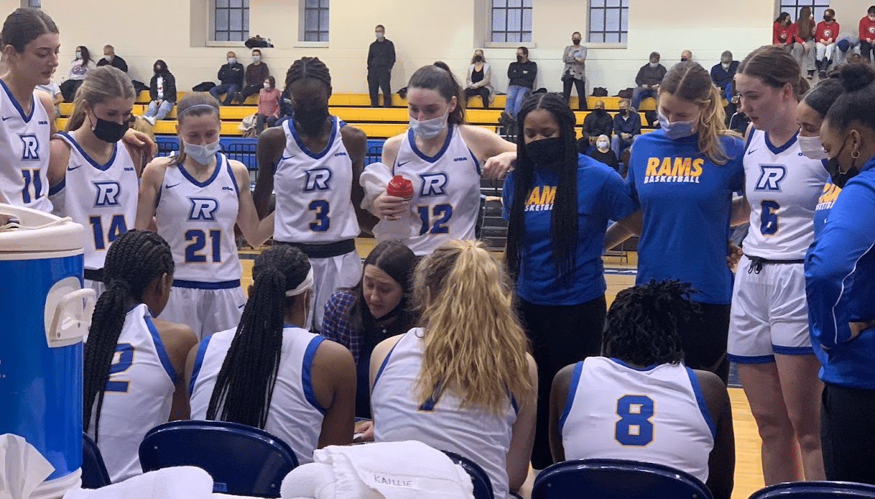 People in white basketball jerseys in a close huddle on a team bench.