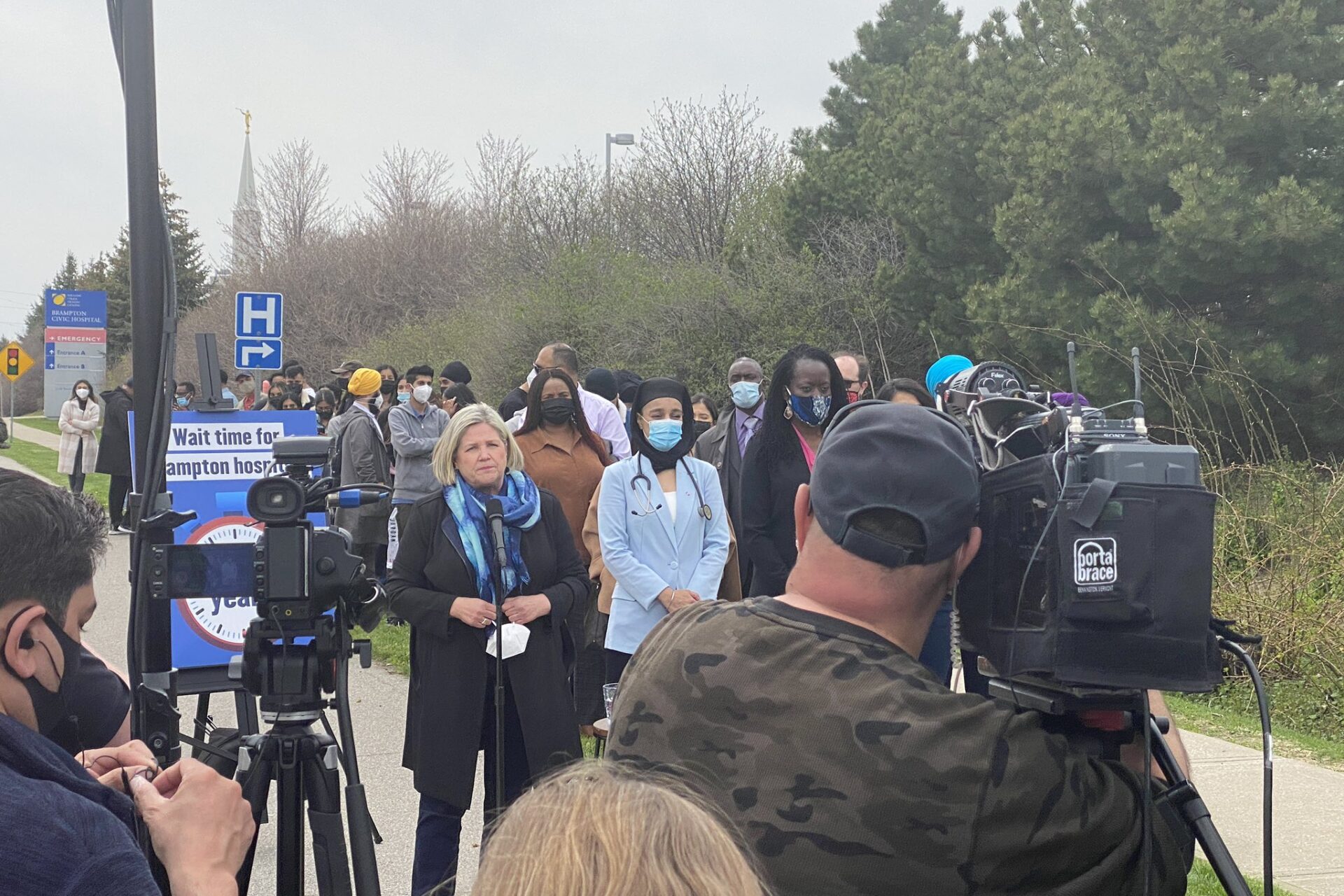 People standing in front of cameras and speaking outside on a sidewalk.