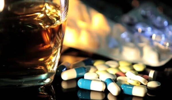 Extreme close up of a glass of whiskey and a handful of blue and white pills