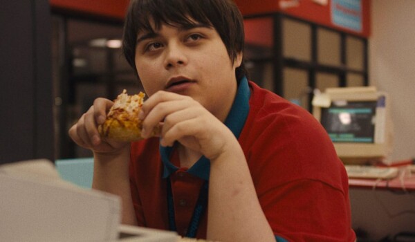 A person wearing a red shirt is holding a dessert as they stares to the left of them.