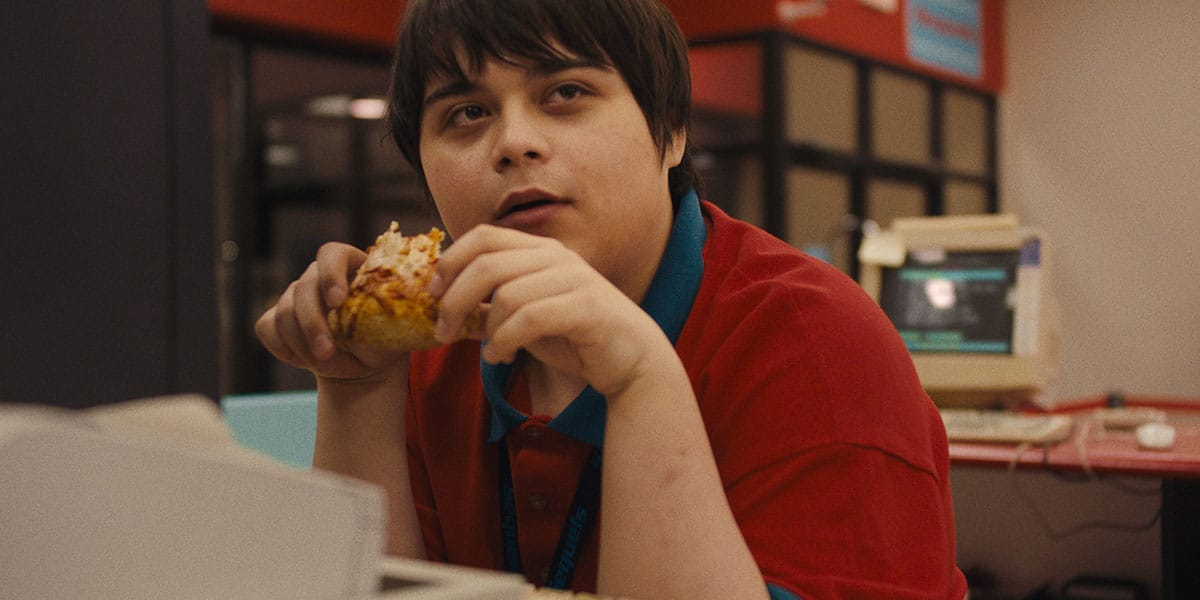 A person wearing a red shirt is holding a dessert as they stares to the left of them.