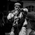 A black and white image of Siddartha. He holds a microphone and is pointing toward the camera.