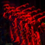 The image edited to be red and black features Siddartha holding a mic out to the audience. The image is overlayed with lower opacity copies of Siddartha.