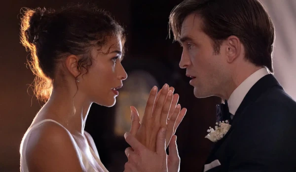 Image from the side of Charlie (Robert Pattinson) holding Emma (Zendaya) by the wrists while they look directly in eachother's eyes, dressed in wedding attire.