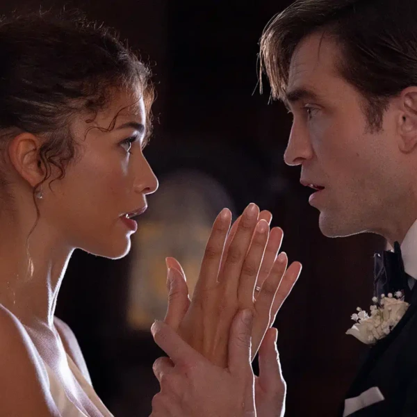 Image from the side of Charlie (Robert Pattinson) holding Emma (Zendaya) by the wrists while they look directly in eachother's eyes, dressed in wedding attire.