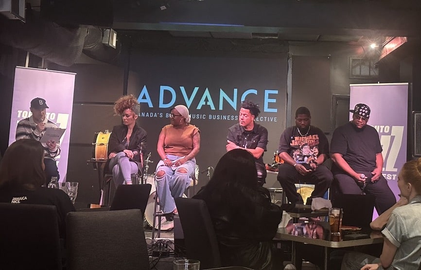 Panelists for a talk sitting on a lit stage in a dark room